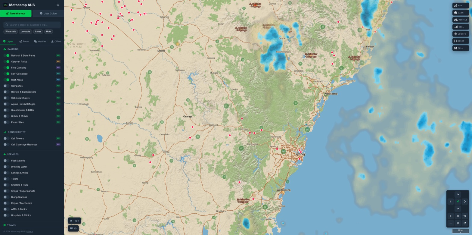 Motocamp Australia showing campgrounds, free camps and caravan parks clustered across New South Wales (Sydney, the Blue Mountains and the Hunter), with live rain radar down the coast and the layer panel open.